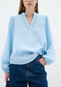 Ljust blå blus med puffärmar, en scallopad halsringning och texturerad ribbning, tillsammans med mörka denimjeans.