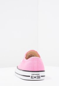 Sneaker in tela rosa con suola in gomma bianca e strisce nere; presenta una punta rotonda, cuciture in contrasto e un logo prominente sul tallone.