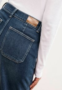 Donkerblauwe spijkerbroek van denim met een leren label met het merk "LIPSY" op de tailleband, voorzien van een enkele achterzak en een slim-fit ontwerp.