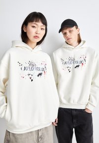 Sweat-shirts blancs avec un graphique à l'avant présentant des éclaboussures de couleur et le texte "JE PEUX TE FAIRE ENTENDRE." Les deux modèles ont des poches kangourou et des ourlets côtelés.
