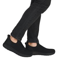 Bottines en mesh noires à enfiler avec un design texturé, semelle flexible et talon rembourré. Portées avec un jean sombre, mettant en valeur le contour de la chaussure.