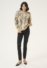 Beige pletený svetr s černými vlnkovými vzory, kombinovaný s černými skinny džíny a černými lodičkami s otevřenou patou. Hladká textura a volný střih.