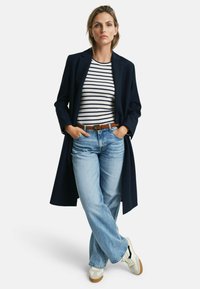 Blazer largo navy sobre una camiseta a rayas negro y blanco, jeans de pierna ancha azul claro y zapatillas beige con acentos negros y suelas de goma.