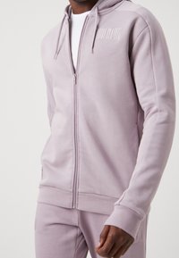 Sudadera con capucha de color lavanda claro con cremallera, confeccionada en tejido suave, que cuenta con cierre frontal de cremallera, dos bolsillos laterales y puños y dobladillo de canalé.