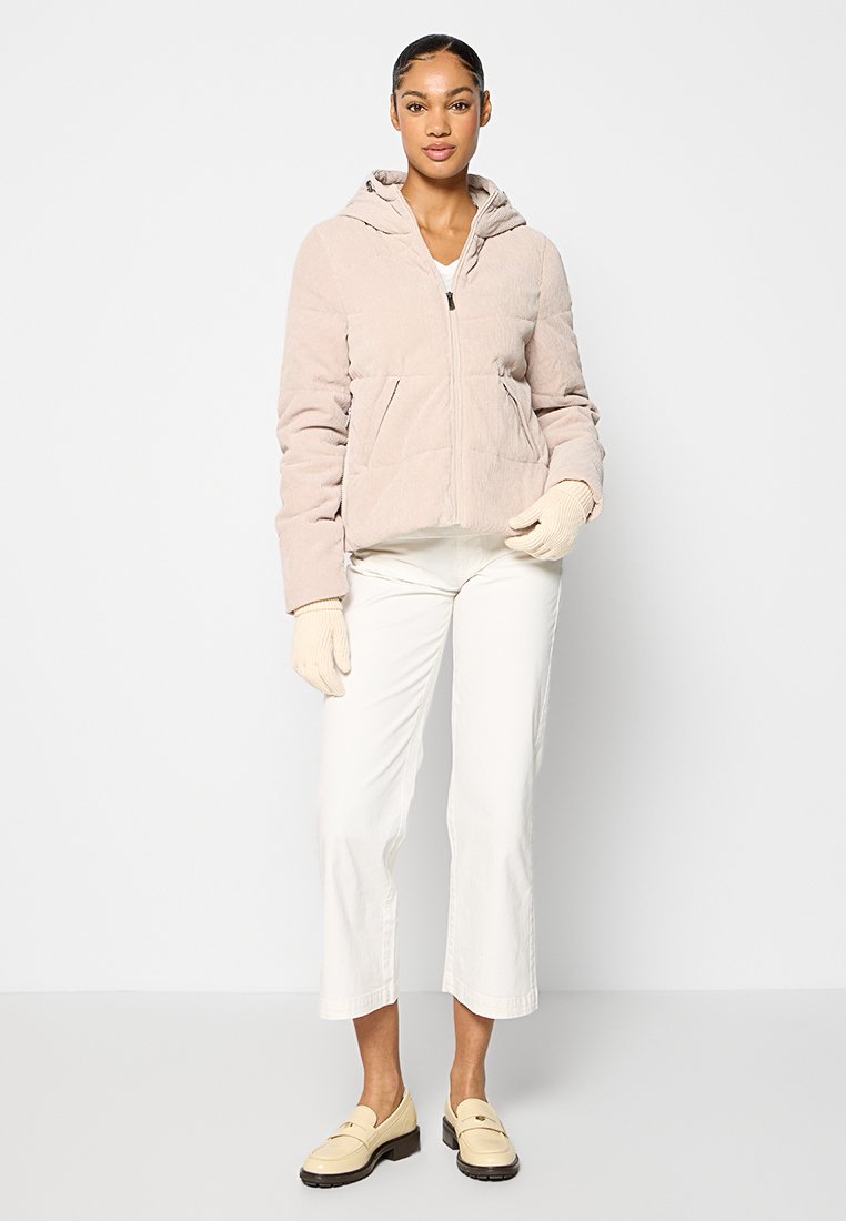 Helle rosa Steppjacke mit Kapuze, ausgestattet mit Fronttaschen und strukturiertem Stoff. Kombiniert mit weißen Hosen und beigen Mokassins.