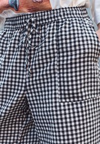 Pantalons à motif vichy noir et blanc avec une taille élastique et un cordon de serrage, dotés d'une poche latérale, fabriqués en tissu léger.