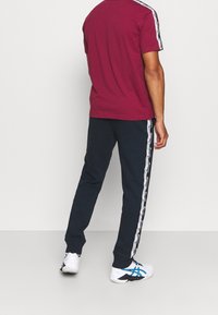 Vinröd t-shirt med rund halsringning i kombination med marinblå träningsbyxor med en vit sidstrimma. Inkluderar logodetaljer och vita atletiska skor.