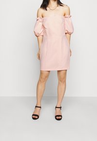 Růžové šaty bez ramínek s nafouknutými rukávy, přiléhavým korzetem a rovnou siluetou. Nosené s černými sandály na vysokém podpatku.