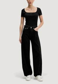 Černý žebrovaný krátký top s hranatým výstřihem, kombinovaný s černými vysokými širokými džíny. Má zapínání na knoflíky a přední kapsy.