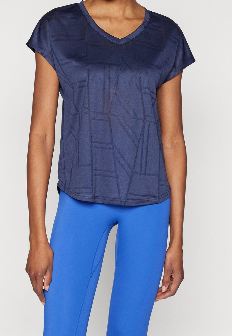 Marinblå v-halsad sportströja med korta ärmar, med ett geometriskt mönster. Kombinationen med ljusblå leggings, mjuk textur och lätt vikt.