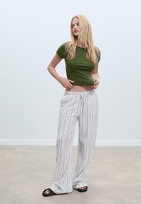 T-shirt aderente verde oliva abbinato a pantaloni ampi a righe leggeri in grigio e bianco, con vita regolabile e vestibilità rilassata.