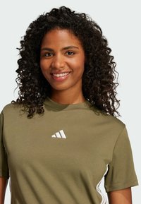 Olive green cotton t-shirt with short sleeves and a crew neckline. Features a white Adidas logo on the left side. Smooth texture.