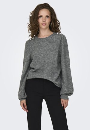 Pull en maille gris avec des manches longues, des poignets côtelés et des accents floraux décoratifs sur l'épaule. Associé à un pantalon noir ajusté.