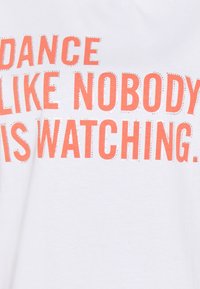 Vit t-shirt med stor, korallfärgad text som säger "DANCE LIKE NOBODY IS WATCHING" i silverdetaljer och en ledig, avslappnad passform.