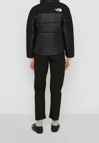 Chaqueta acolchada negra con diseño acolchado, que presenta un cuello alto y acentos de logo, combinada con pantalones negros ajustados y calzado oscuro.