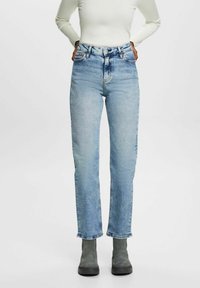 Jeans de tiro alto en azul claro, fabricados en denim, con piernas rectas y un sutil desgaste. Combinados con botas de tobillo gris.