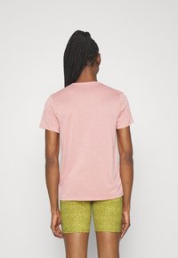 Camiseta de manga corta y cuello redondo en tejido rosa claro, combinada con pantalones cortos verdes con estampado. Enfoque en un diseño y ajuste simples y atléticos.