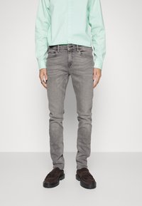 Jeans de mezclilla gris con corte slim, con cinco bolsillos y un ligero desgaste. Combinados con una camisa de botones verde claro y mocasines marrones.