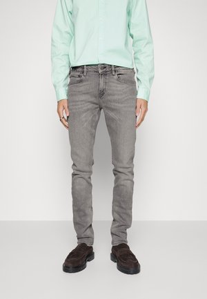 Graue Denim-Jeans mit Slim Fit, fünf Taschen und leichter Ausbleichung. Kombiniert mit einem hellgrünen Hemd mit Knöpfen und braunen Slippern.