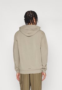 Felpa con cappuccio beige a vestibilità rilassata, in tessuto texturizzato e con polsini a costine. Presenta un piccolo logo nella parte bassa della schiena.