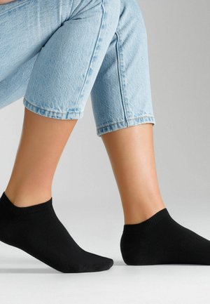 Czarne skarpetki za kostkę na stopach, o miękkiej fakturze, z prążkowanym mankietem i dopasowanym krojem, zestawione z jasnoniebieskimi, podwiniętymi jeansami.