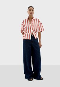 Red and white striped short-sleeve shirt with a buttoned front, paired with wide-leg dark denim pants and black sandals.