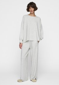 Felpa grigia chiara e pantaloni abbinati. Tessuto morbido e testurizzato; vestibilità rilassata con polsini a costine e vita regolabile con cordoncino. Dettaglio del logo discreto.