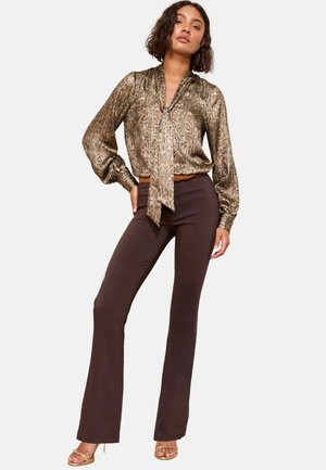 Blusa bronzo con stampa a serpente e colletto con fiocco; maniche lunghe a palloncino abbinate a pantaloni a zampa d'elefante marroni e sandali metallici con fascia.