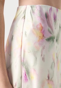 Gros plan d'une jupe taille haute avec un imprimé floral aquarelle pastel dans des tons de rose, jaune et vert sur un fond clair.