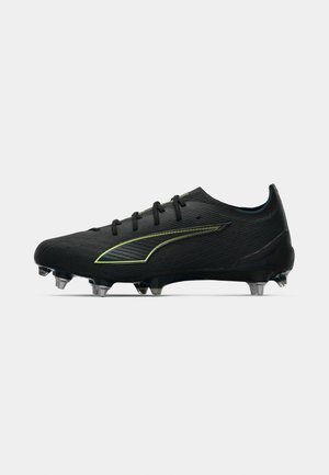 Botín de fútbol negro con una superficie texturizada, acentos verdes, cordones centrales y tacos cónicos para una mejor tracción.