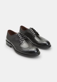 Scarpe da cerimonia in pelle nera con punta arrotondata, dettagli brogue intricati e chiusura con lacci. Tacco rinforzato e finitura liscia.