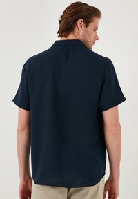 Korte mouwen, marineblauw shirt van lichtgewicht stof. Kenmerkt zich door een campkraag en een losse pasvorm met een rechte zoom en subtiele textuur.