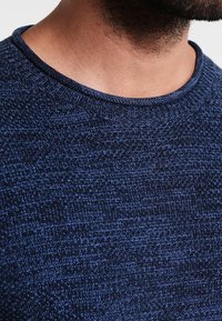 Navy blue knitted sweater featuring a round neckline and textured fabric, showcasing a subtle pattern and ribbed cuffs.
