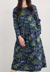 Mörkblå långärmad klänning med grön och vit botanisk tryck, med skiktad kjol och två sidofickor. Bomullstextur.