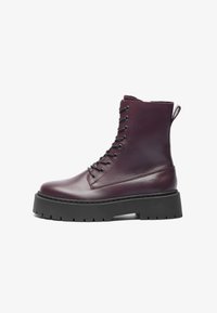 Bottes en cuir bourgogne à lacets avec une tige haute, semelle épaisse noire et bout rond. Elles disposent d'une languette à l'arrière et d'un laçage avec œillets.