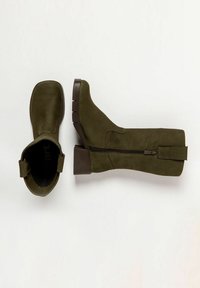Un par de botas verde oliva hasta medio pantorrilla con cremallera lateral y tacones bajos en marrón, exhibidas sobre un fondo blanco.