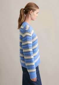 Sweter robiony na drutach w niebieskie, białe i zielone paski. Posiada luźny krój, ściągacze u rękawów i otwartą teksturę dzianiny.