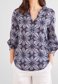 Camicia blu navy in tessuto leggero, con un motivo a foglie bianche, mezza fila di bottoni e maniche a tre quarti con risvolti.