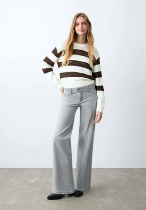 Neulepaidassa on valkoisia ja ruskeita vaakaraitoja, neulottu pintakuvio. Malli käyttää vaaleanharmaita leveälahkeisia housuja, joissa on etutaskut, sekä mustia jalkineita.