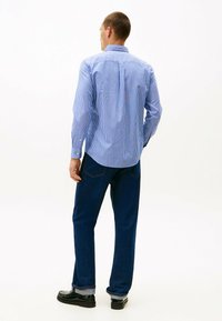 Blå og hvid striped knap-up skjorte med lange ærmer, parret med mørkeblå jeans og sorte sko, set fra ryggen.