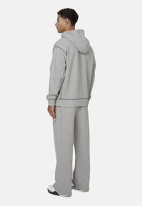 Felpa con cappuccio grigia e pantaloni coordinati realizzati in un tessuto morbido. Vestibilità ampia con dettagli di cucitura discreti e un design rilassato.