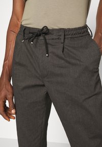 Pantalons taillés gris foncé avec une taille élastique, cordon de serrage ajustable et poches latérales, présentant un tissu texturé subtile.