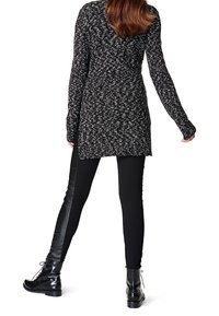 Tunique tricotée noir et blanc mouchetée avec des manches longues, associée à des leggings noirs avec un panneau en cuir et des bottines noires à lacets.