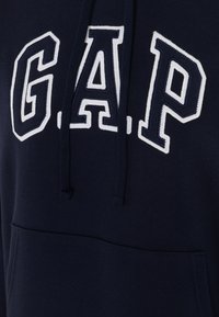 Navy blue hoodie with a kangaroo pocket, featuring large white "G.A.P." lettering on the front and a drawstring hood. Soft texture.