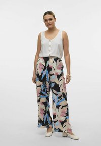 Witte, mouwloze top met knopen, gecombineerd met wijde zwarte broek met roze en blauwe bloemenprints. Textuurstof en losse pasvorm.