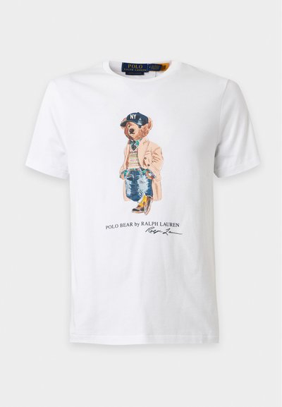 T-shirt blanc avec un ours portant un manteau beige, un pull à carreaux, un jean, des bottes et une casquette NY bleu marine avec le texte ""Polo Bear by Ralph Lauren"".