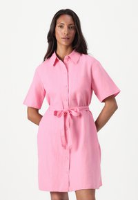 Kortermet, knappet kjole i rosa lin, med belte i midjen og en frontlomme. Lett og luftig design med klassisk krage.