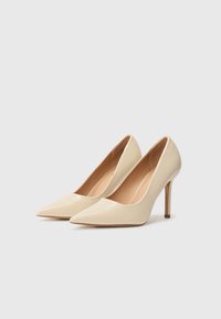 Scarpe con tacco alto beige, con punta appuntita, realizzate in materiale sintetico liscio e con un tacco a stiletto sottile e metallico.