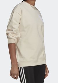 Light beige sweatshirt with a relaxed fit, ribbed cuffs, and a crew neckline. Features subtle branding on the chest. Cotton blend material.