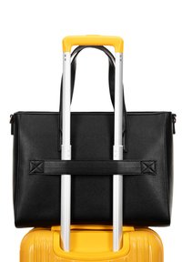 Schwarze, strukturierte Leder-Tote-Tasche, die auf einem gelben Koffer platziert ist, mit silbernen Metallgriffen und einem Schultergurt.